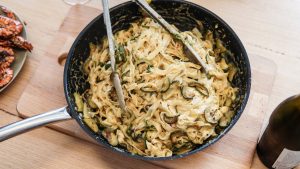 Overhead view of creamy zucchini pasta in a rustic pan on a wooden table, perfect for gourmet dining.