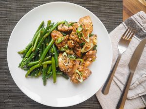 A delicious serving of sesame chicken with fresh green beans on a white plate, perfect for dinner.