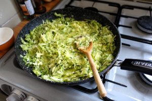 Freshly shredded zucchini cooking in a frying pan on a modern kitchen stove.
