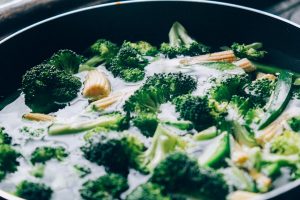 Close-up of fresh broccoli and baby corn sizzling in a pan for a healthy meal.