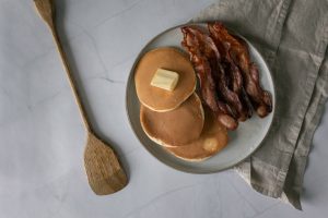 Top view of a breakfast plate with buttery pancakes and crispy bacon on a marble surface.