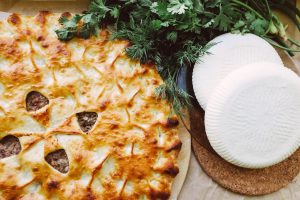Savory baked cheese pie with a golden crust, accompanied by fresh herbs and cheese wheels.