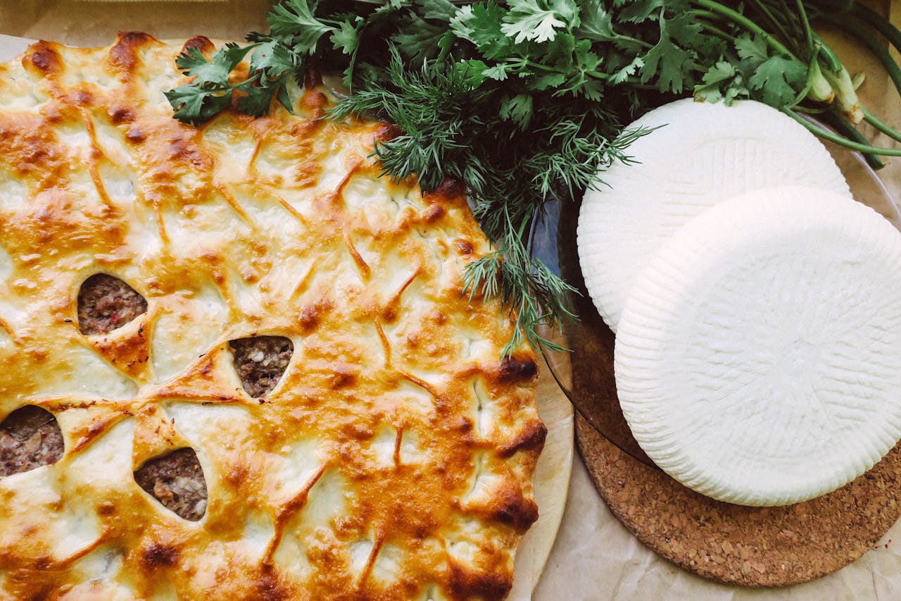 Savory baked cheese pie with a golden crust, accompanied by fresh herbs and cheese wheels.